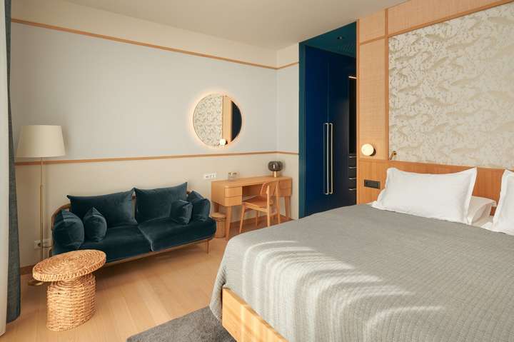 Luxurious bedroom suite with a king-size bed, elegant patterned wallpaper, a plush blue velvet sofa, and custom cabinetry.