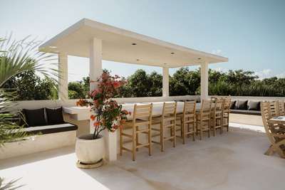 High-end rooftop bar at Villa Imperia with a sleek white counter, wooden stools, and shaded lounge amidst tropical plants.