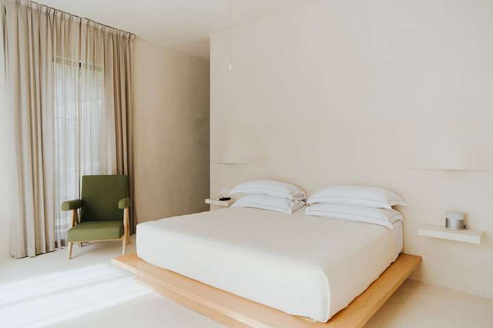Serene minimalist bedroom in Tulum featuring a wooden platform bed, crisp white linens, and elegant sheer curtains.