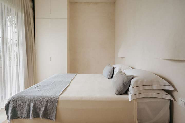 Luxury Tulum villa bedroom showcasing a minimalist wooden platform bed, premium linens, and custom built-in closets.