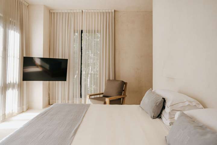 Luxury master suite in Tulum villa featuring minimalist decor, plush bedding, sheer curtains, and a flat-screen TV.