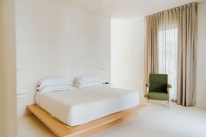 Minimalist master suite at Villa Imperia featuring a wooden platform bed, elegant white linens, and tropical views.