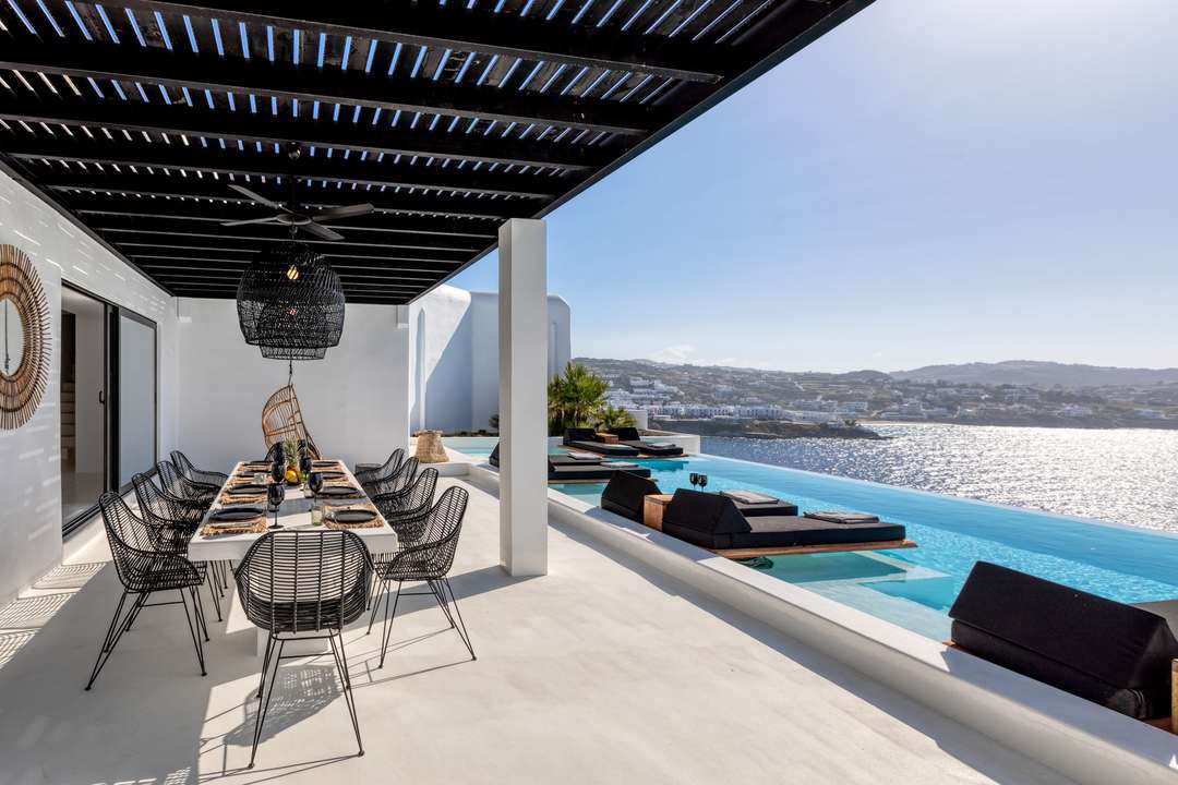 Elegant alfresco dining under a pergola at Villa La Isla in Mykonos, featuring an infinity pool and sweeping sea views.