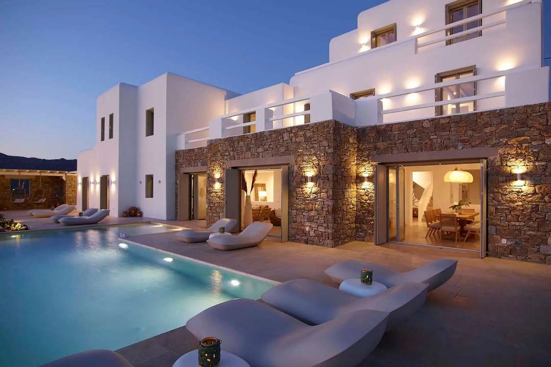 Evening at luxury Villa Mariza featuring Cycladic whitewashed walls, local stone, and a private illuminated infinity pool.
