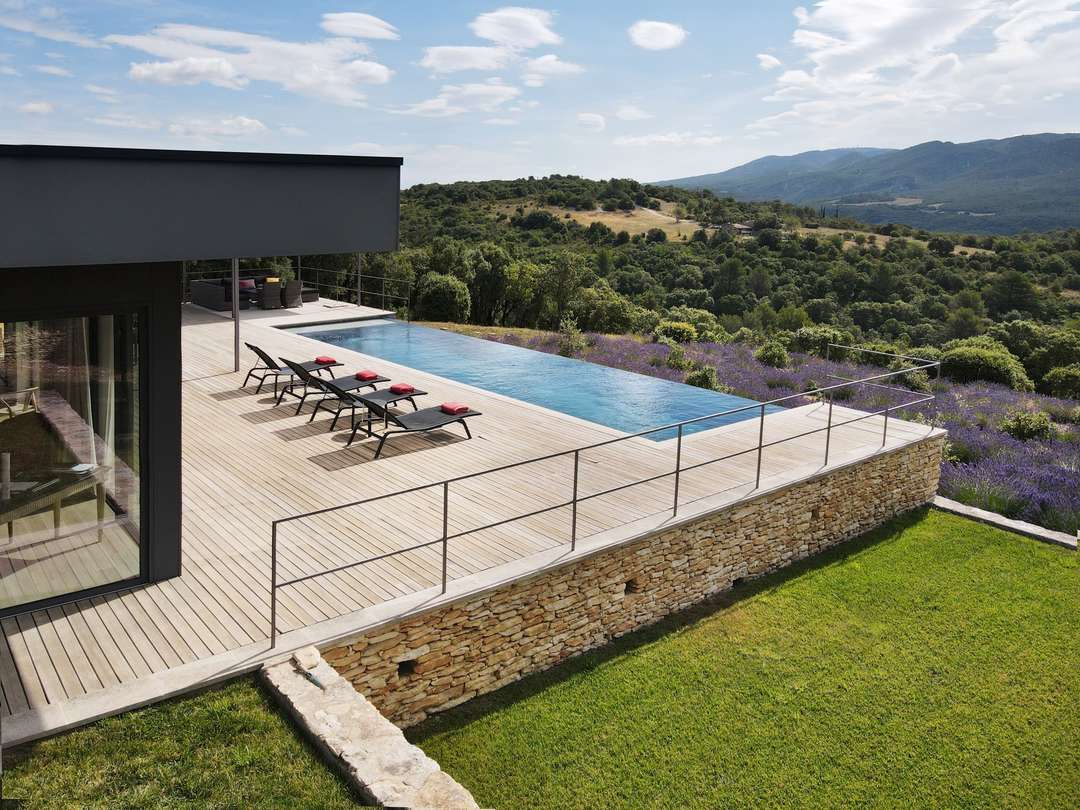 Sleek infinity pool and wooden deck at Villa Melodie, offering panoramic Luberon mountain views over lush lavender fields.