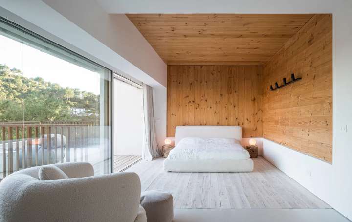 Luxury bedroom with natural wood finishes, plush white bed, and scenic forest views at Villa Natura in El Madroñal.