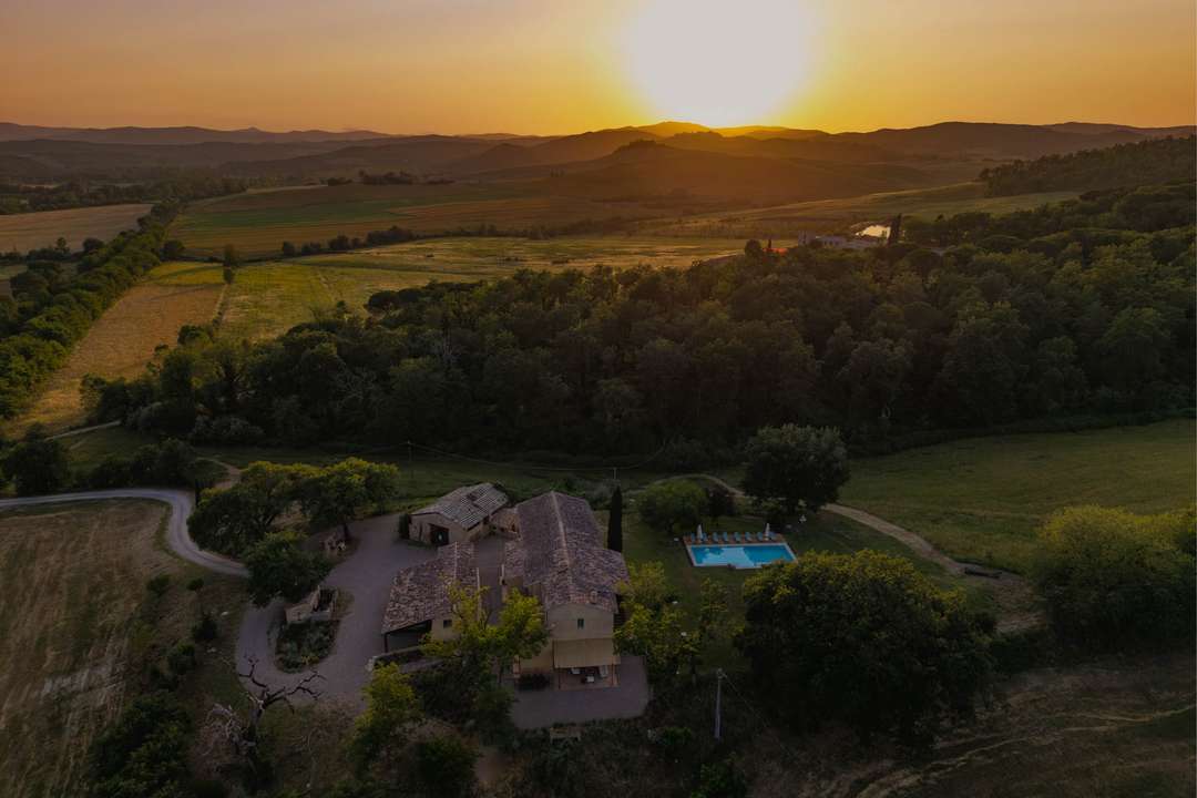 Aerial sunset view of luxury Villa Pacera in Tuscany, featuring a private pool and sweeping Val d'Orcia views.