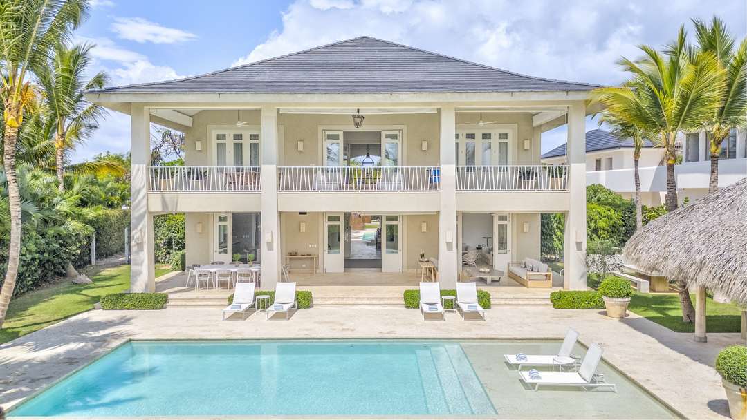 Elegant two-story villa facade with a private pool, covered dining terrace, and a thatched palapa amidst lush greenery.