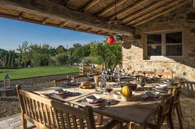 Covered outdoor dining terrace at Villa Poderosa with a long wooden table, stone walls, and views of the manicured garden.