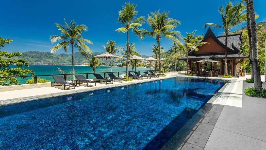 Expansive infinity pool at Villa Purissara featuring sun loungers, palm trees, and panoramic Andaman Sea views in Phuket.