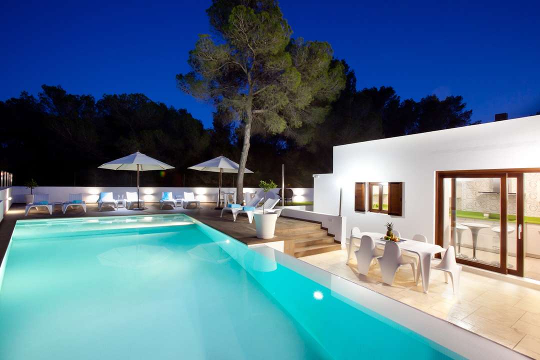 Illuminated saltwater infinity pool at night with sun terrace, loungers, and alfresco dining area at a luxury Ibiza villa.