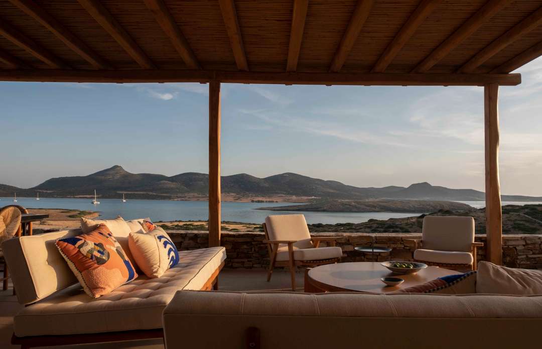 Elegant shaded outdoor lounge at Villa Tyche with plush seating, wooden pergola, and panoramic Aegean Sea views.