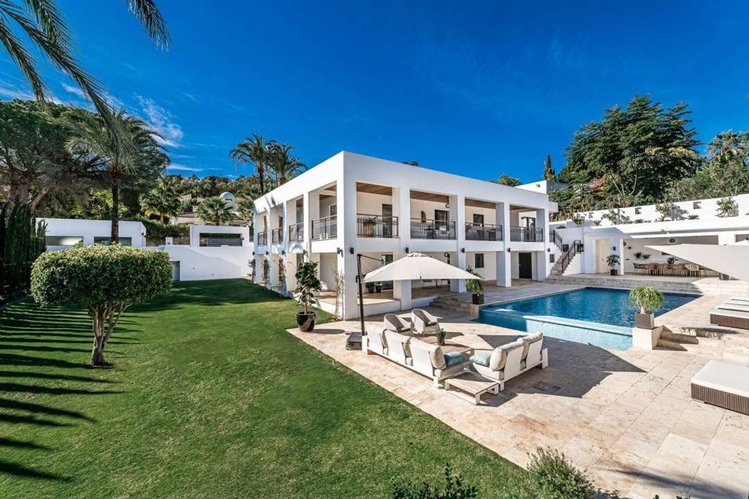 Contemporary white facade of Villa Unai in Nueva Andalucia, featuring a manicured lawn, wrap-around terrace, and private pool.