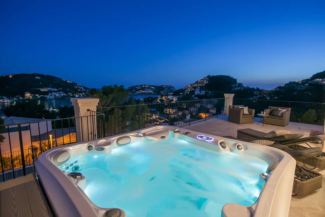 Six-person hot tub at Villa Willow, offering sweeping night views of Port d'Andratx marina and the illuminated hillside.
