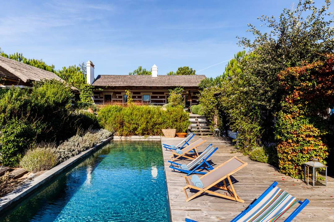 Serene private pool and wooden deck at Villa Yuki, featuring traditional thatched-roof Comporta architecture and lush gardens.