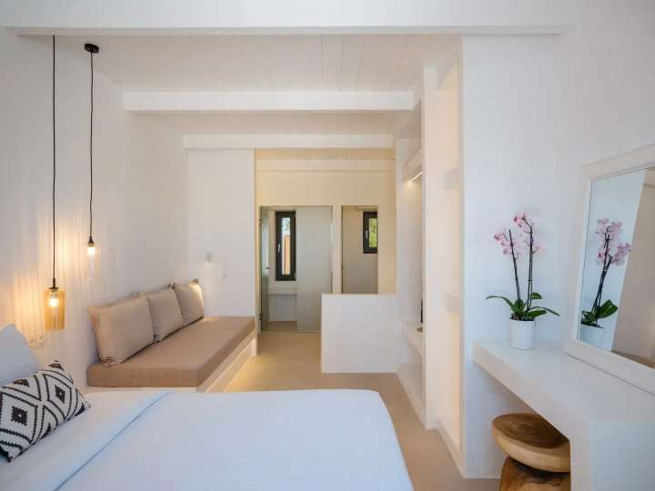 Serene luxury bedroom at Olive & Vines featuring minimalist white decor, a built-in lounge sofa, and elegant pendant lighting.