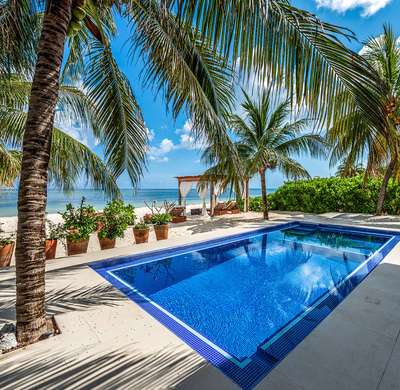 Stunning private blue-tiled pool surrounded by tropical palm trees, offering seamless views of the white-sand beach and sea.