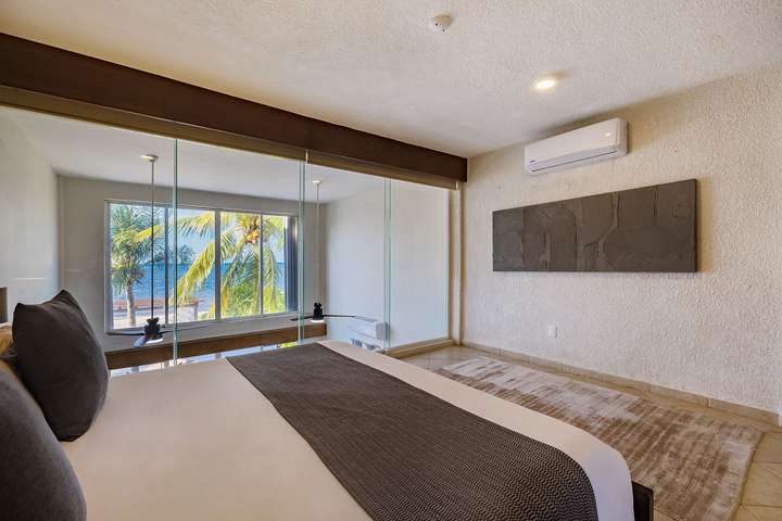 Chic oceanview bedroom at Villas Solil in Cozumel featuring expansive glass windows, plush bedding, and tropical vistas.