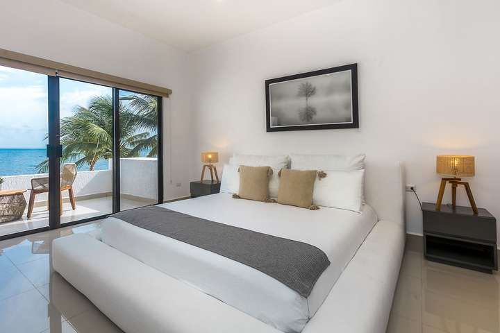 Bright and airy master suite at Villas Solil with a plush white bed and sliding doors opening to a stunning ocean view.
