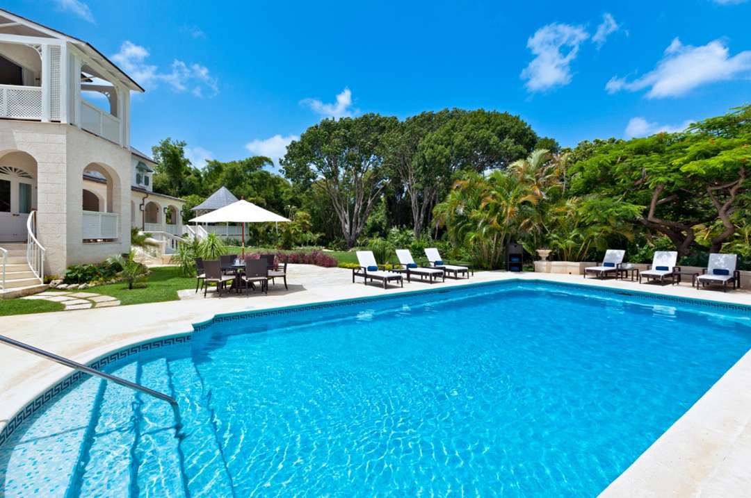 Large private swimming pool with coral stone deck, sun loungers, and lush tropical gardens at Windward luxury villa.