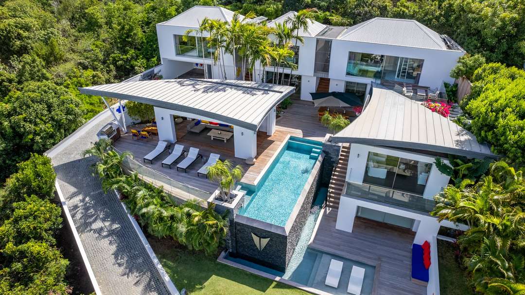 Aerial view of Villa Wings in St. Barths, showcasing unique wing-shaped roofs, a heated infinity pool, and lush gardens.
