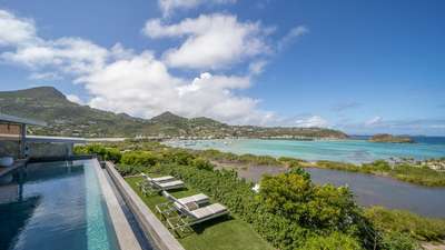 Serene manicured lawn with comfortable sun loungers beside the infinity pool, overlooking the shimmering St. Barths lagoon.